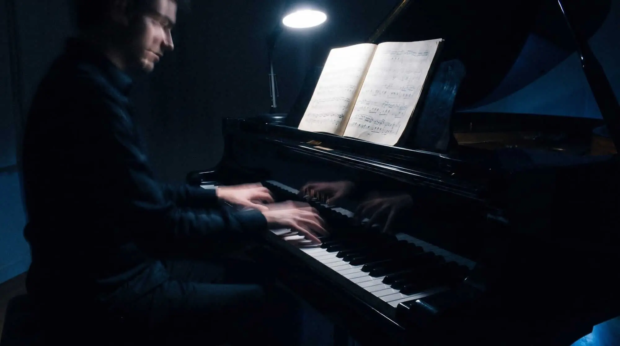 Pianista actuando en un piano de cola mientras lee partitura en un estudio oscuro.